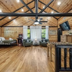 Open loft with a bed, a gray sofa, green armchairs, an arcade basketball game and a foosball table under a vaulted ceiling