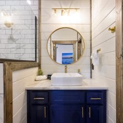Round mirror reflecting a lake print above a gold faucet