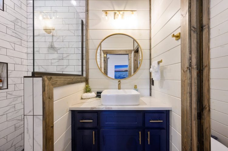 Round mirror reflecting a lake print above a gold faucet