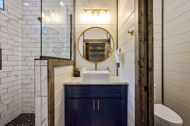 Round gold mirror reflecting a reclaimed wood wall above a vessel sink