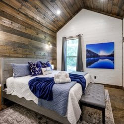 Bed with a blue quilt and rolled towels, a reclaimed wood accent wall and a Welcome pillow