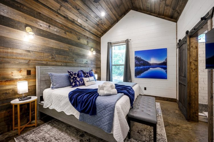 Bed with a blue quilt and rolled towels, a reclaimed wood accent wall and a Welcome pillow