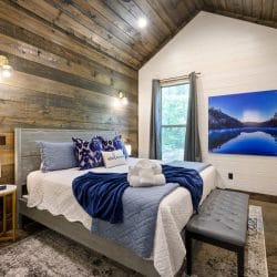 Bed with a blue patterned Welcome pillow, a lamp and a reclaimed wood wall