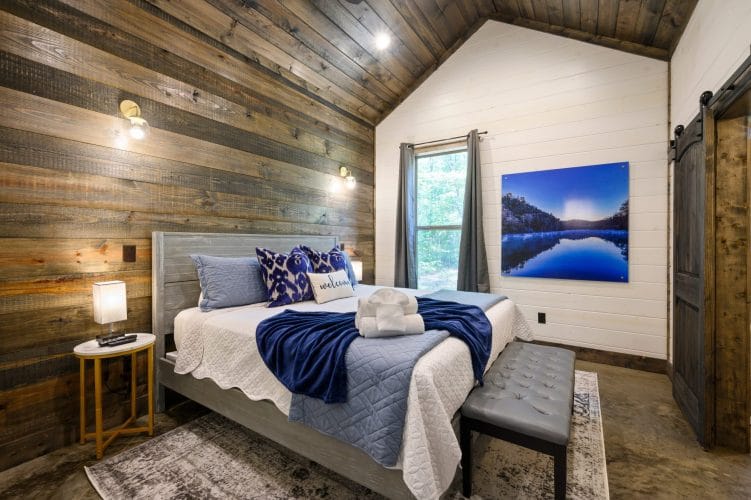 Bed with a blue patterned Welcome pillow, a lamp and a reclaimed wood wall