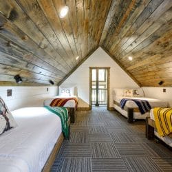 Upstairs room with beds under a vaulted wood ceiling and a balcony door