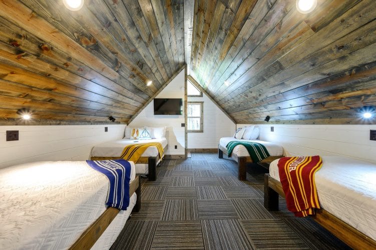 Upstairs bed with a yellow throw, a wall TV and a window under the vaulted ceiling