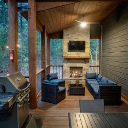 Covered porch with a stone fireplace, TV above the mantel and blue cushioned seating