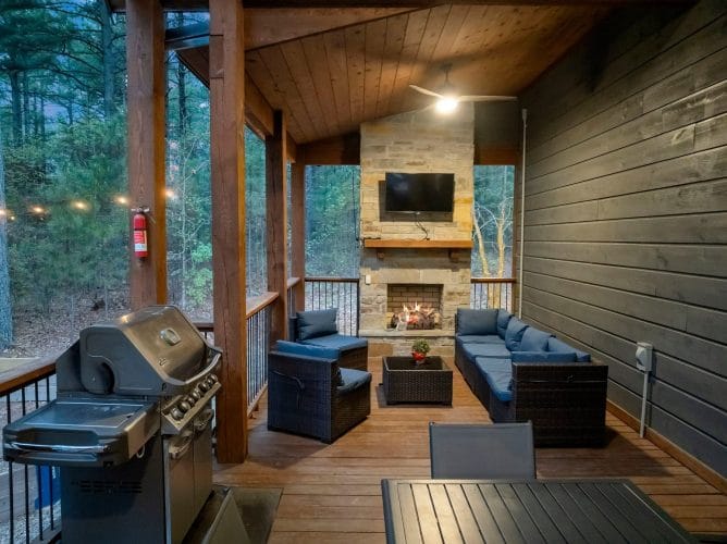 Covered porch with a stone fireplace, TV above the mantel and blue cushioned seating