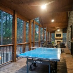 Covered porch with timber posts, string lights and a gas grill with a table in the distance