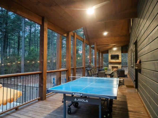Covered porch with timber posts, string lights and a gas grill with a table in the distance