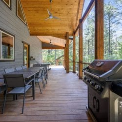 Long covered porch with a dining table, chairs and a gas grill