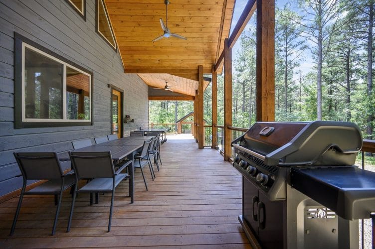 Long covered porch with a dining table, chairs and a gas grill
