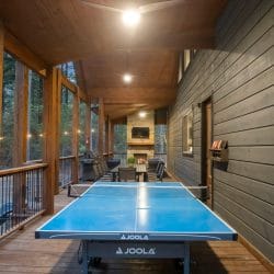 Covered porch at dusk with a dining table, a stone fireplace with TV and a grill