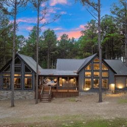 Back of the cabin at dusk with lit windows and the covered porch