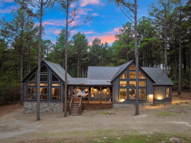Back of the cabin at dusk with lit windows and the covered porch