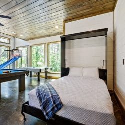 Murphy bed folded down with a white quilted cover and plaid blanket, with the air hockey table by the window