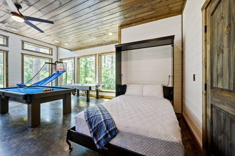 Murphy bed folded down with a white quilted cover and plaid blanket, with the air hockey table by the window