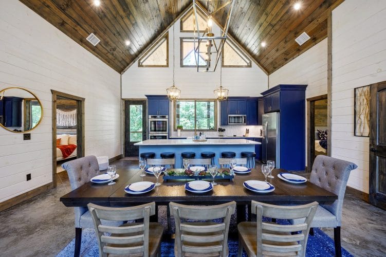 Blue kitchen island with white counters, a gold faucet and a wall oven under a window