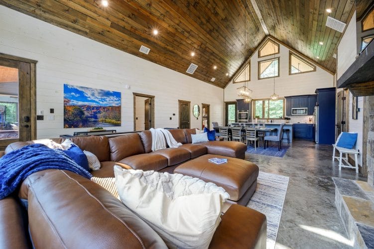 Brown leather sectional with blue and striped pillows and a wood door behind it