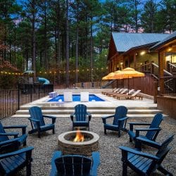 Backyard pool at dusk with blue Adirondack chairs, loungers, orange umbrellas and string lights
