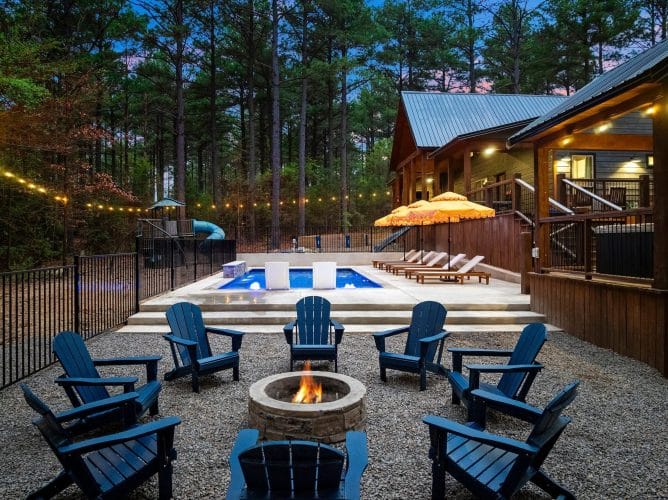 Backyard pool at dusk with blue Adirondack chairs, loungers, orange umbrellas and string lights