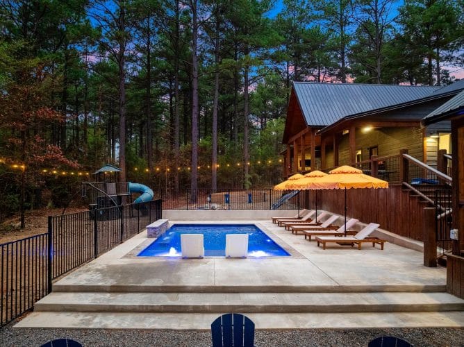 Pool edge with a black safety fence, string lights and a slide behind it