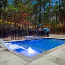 Pool with a stone water feature and the playset behind the fence