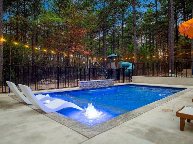 Pool with a stone water feature and the playset behind the fence