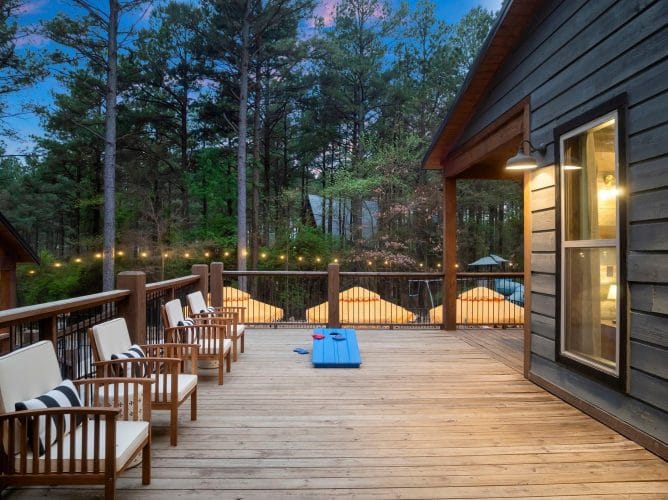 String lights and umbrellas along the deck railing with a rooftop peak in the trees