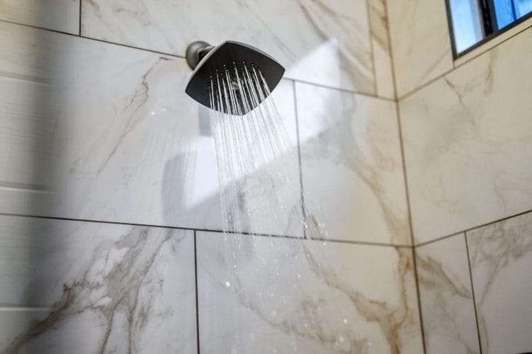 Water spraying from the shower head against white tile