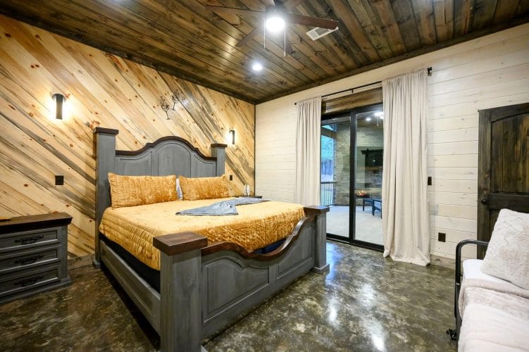 Bed with a gray carved headboard and gold velvet bedspread, with a glass door to the patio