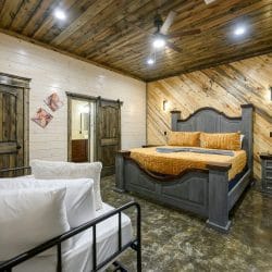 Foot of the bed with gold bedspread beside a wood door and the bathroom vanity