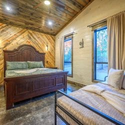 Dark wood bed with green bedding next to a window, with a black metal daybed in the foreground