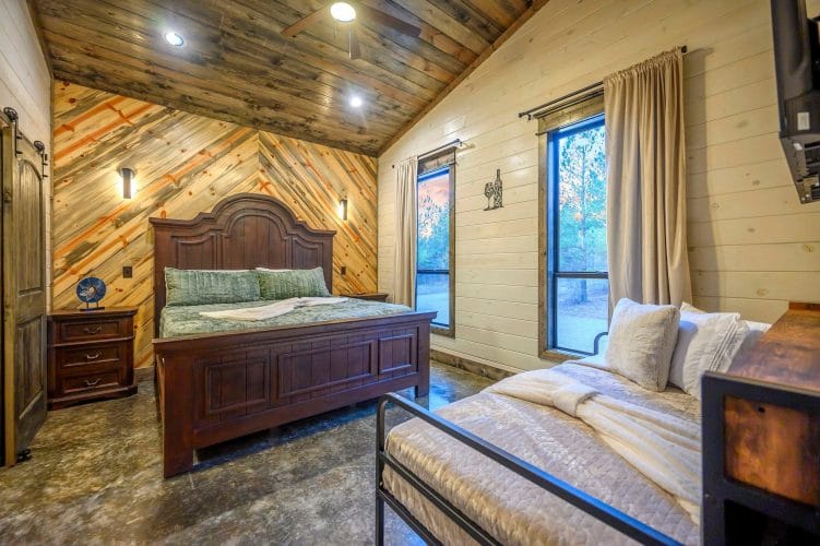 Dark wood bed with green bedding next to a window, with a black metal daybed in the foreground
