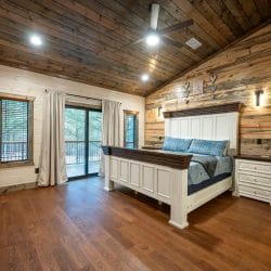 Bed with a white headboard and blue velvet bedding beside a glass balcony door