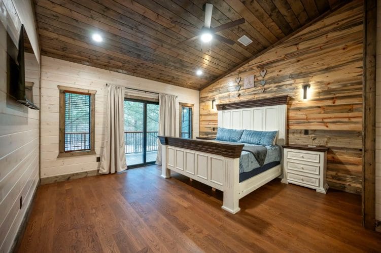 Bed with a white headboard and blue velvet bedding beside a glass balcony door
