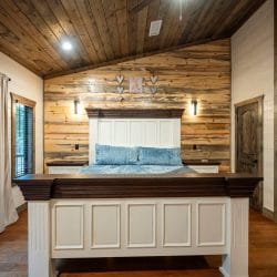 White paneled headboard with blue velvet pillows against a reclaimed wood wall