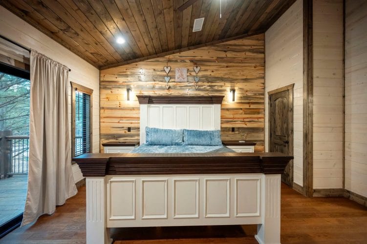 White paneled headboard with blue velvet pillows against a reclaimed wood wall