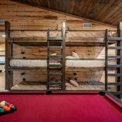 Triple-stacked bunk beds with a ladder behind a red-felt pool table
