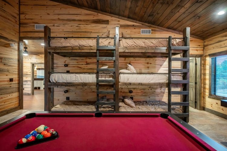 Triple-stacked bunk beds with a ladder behind a red-felt pool table