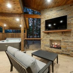 Stone outdoor fireplace with a TV on the mantel and a deck railing