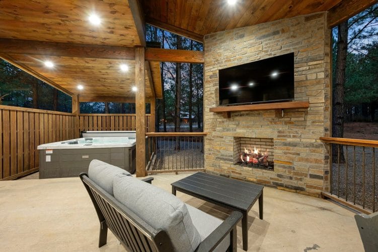 Stone outdoor fireplace with a TV on the mantel and a deck railing