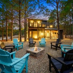 Fire pit glowing at night with teal and black Adirondack chairs and the lit patio behind