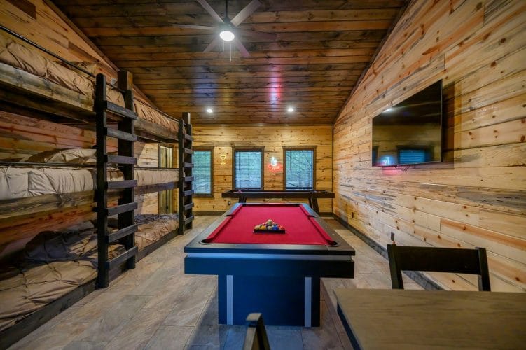 Red-felt pool table and shuffleboard under three windows with a neon wine sign