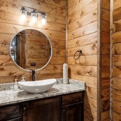 Vanity with a white vessel sink and round mirror against wood-paneled walls
