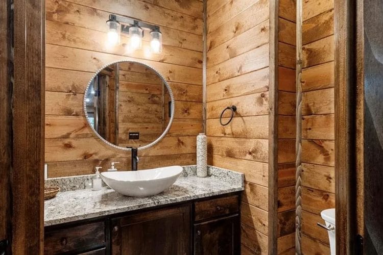 Vanity with a white vessel sink and round mirror against wood-paneled walls