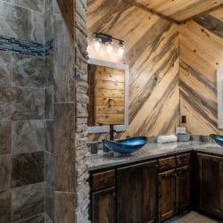 Double vanity with blue vessel sinks next to a tiled walk-in shower