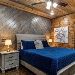 King bed with a navy quilt and gray wood headboard, nightstands with lamps, open door to the bathroom on the right