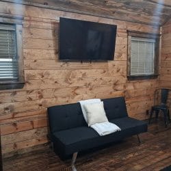 Black futon sleeper under a wall-mounted TV in a bedroom, with a metal chair beside it
