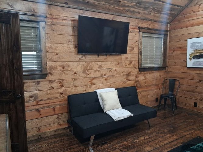 Black futon sleeper under a wall-mounted TV in a bedroom, with a metal chair beside it